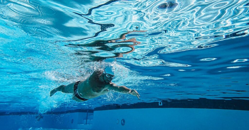 Dynamic underwater photo of a man swimming freestyle in a pool wearing goggles and a cap.